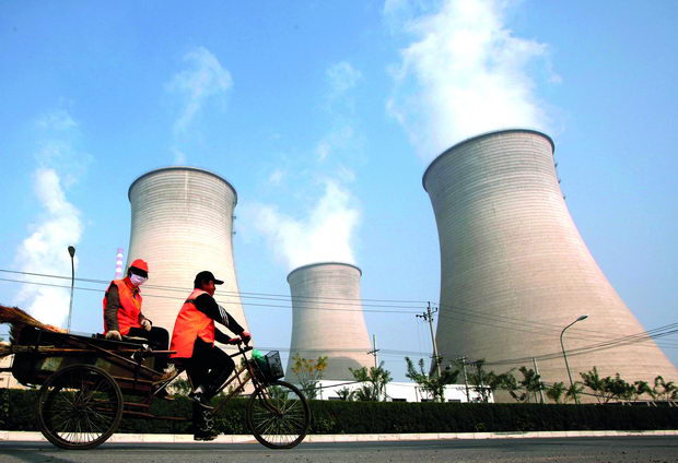 Street cleaners ride their motorised tricycles past the chimneys of a power station located on the outskirts of Beijing