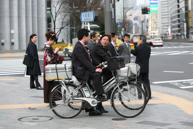 Japanese people stand at a crosswalk waiting for the green traffic light