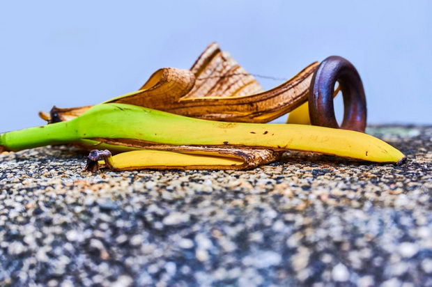 View to a banana peel lying on a concrete bollard with pebbles next to a metal ring.