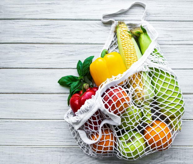 Fresh vegetables and fruits on eco string bag on a white wooden background. Healthy lifestyle. Top view. Zero waste.