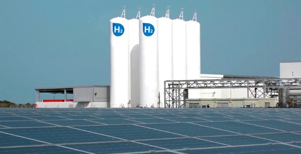 Close-up of a solar panel, in the background a green hydrogen production plant, and also, several hydrogen storage tanks.